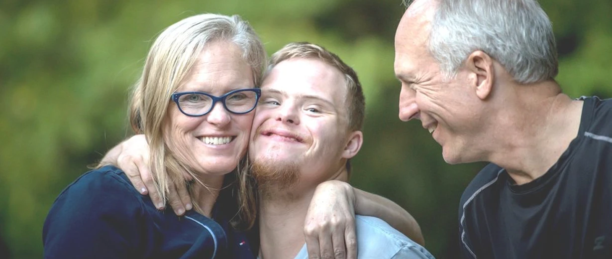 Smiling parents with their son with Down syndrome in a green environment.