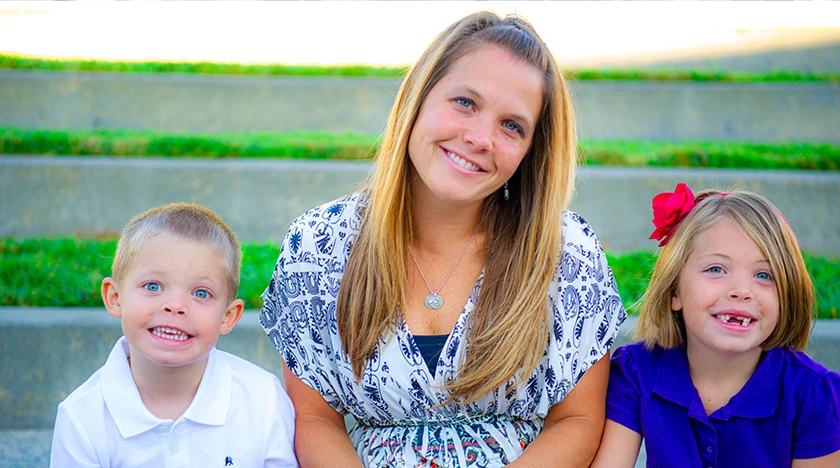 Smiling mother with her two children in a grassy outdoor setting.