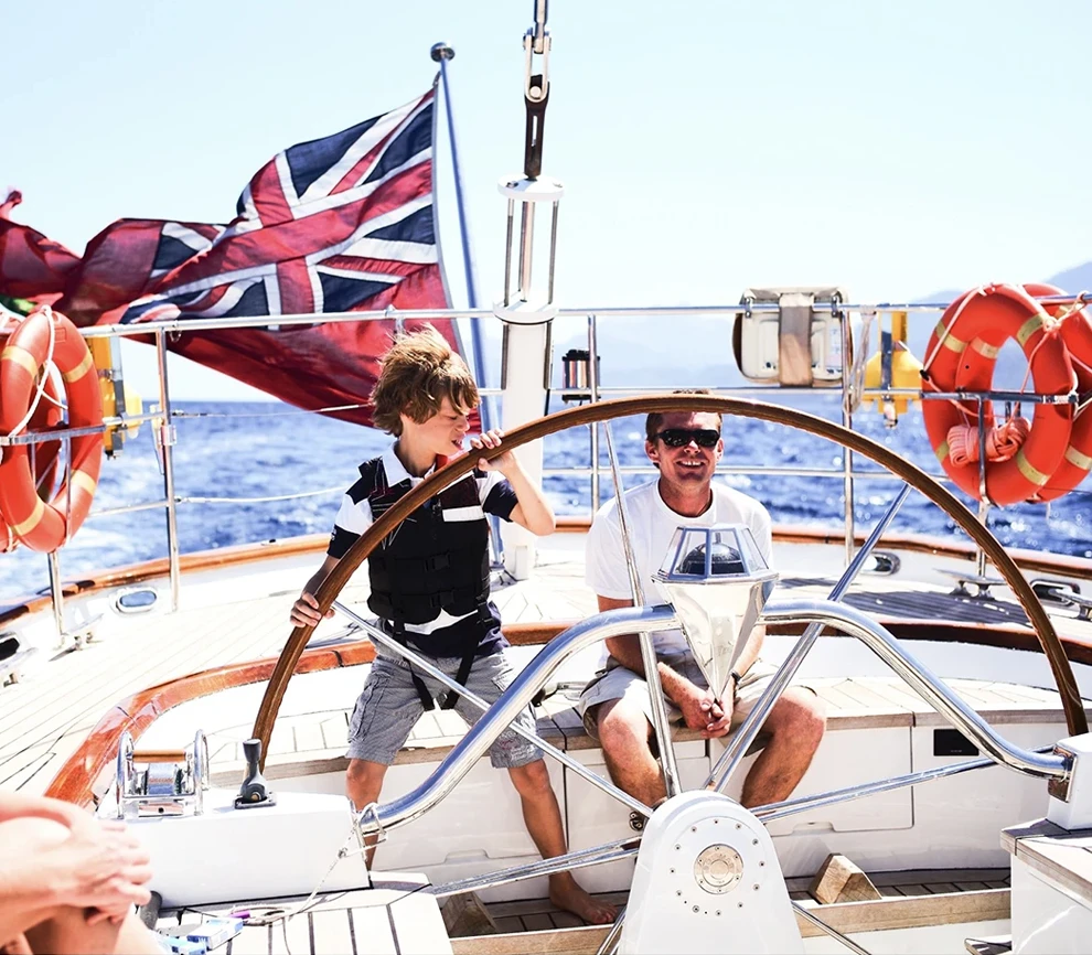 Young boy steering a fast sailing boat under a blue sky in the Mediterranean Sea.